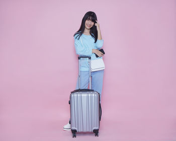 Full length portrait of woman standing against pink background