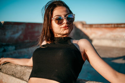 Portrait of young woman wearing sunglasses standing against sky