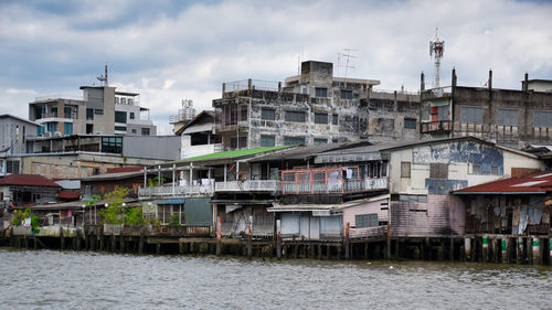 Residential buildings by river against sky in town