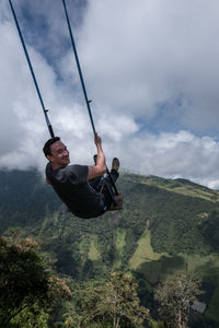 Happy man swinging over mountain at casa del arbol against sky