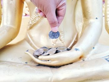 Cropped hand holding coins over statue