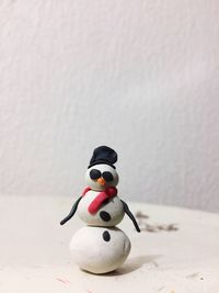 Close-up of artificial snowman on table against wall