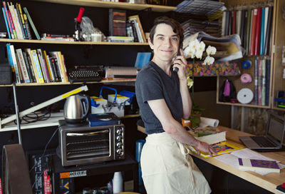 Side view portrait of smiling young man using cordless phone while standing at home office