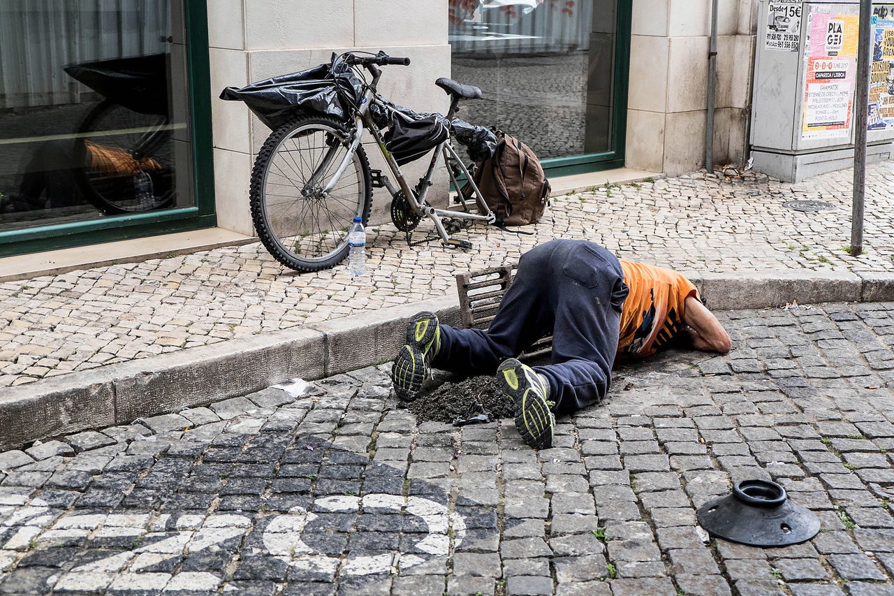 MAN SLEEPING ON SIDEWALK AGAINST BUILDING