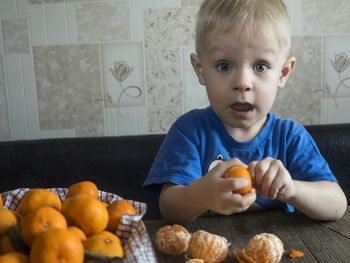 Surprised boy having oranges while sitting on sofa at home