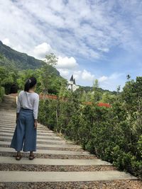 Rear view of woman standing by plants against sky