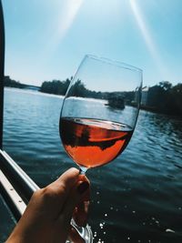 Close-up of hand holding wineglass against river during sunset