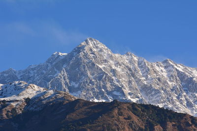 Low angle view of snowcapped mountains against clear blue sky