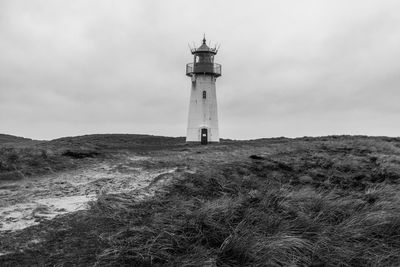 Low angle view of lighthouse on field by building against sky