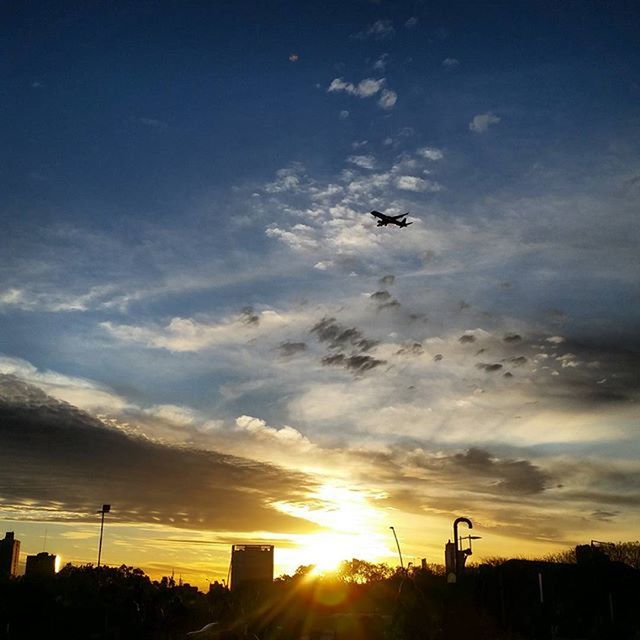 sunset, silhouette, sun, sky, cloud - sky, orange color, sunlight, sunbeam, cloud, built structure, beauty in nature, building exterior, low angle view, scenics, nature, architecture, lens flare, flying, outdoors, bird