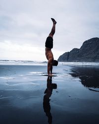 Full length of man doing handstand at beach against sky