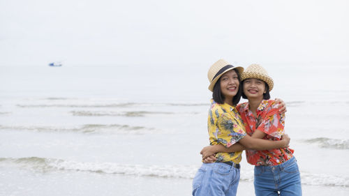 Cute friends embracing while standing against sea