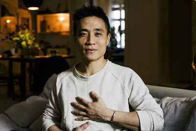 Portrait of man with hand on chest meditating at home