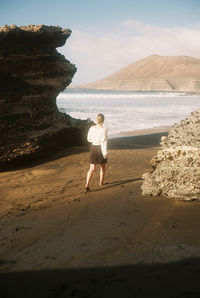 Full length of woman standing on rock at beach against sky