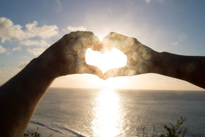 Close-up of hand holding heart shape in sea against sky