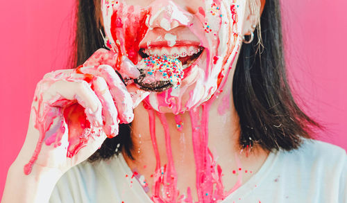 Midsection of woman eating sweet food against pink background