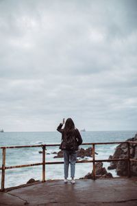 Rear view of woman standing on railing against sea