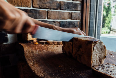 Cropped hand cutting bread loaf on table