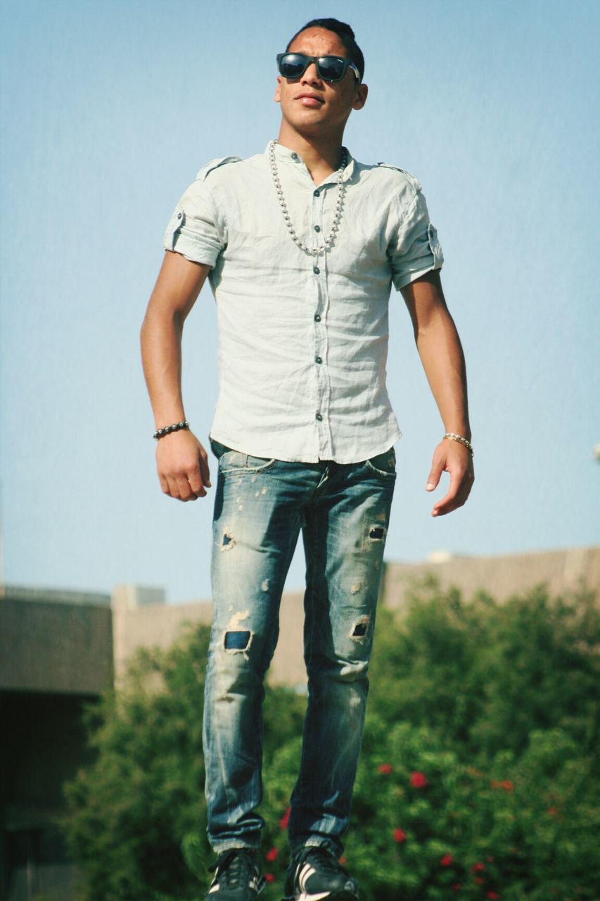 casual clothing, young adult, person, lifestyles, standing, front view, looking at camera, leisure activity, young men, portrait, three quarter length, smiling, full length, sunglasses, hands in pockets, focus on foreground