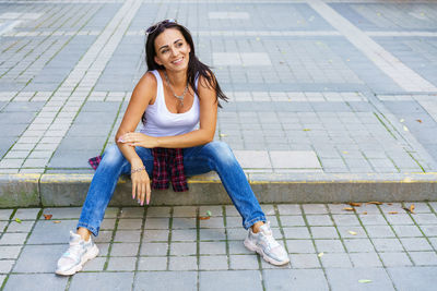 Outdoors lifestyle fashion portrait of contented young woman sitting outdoors.