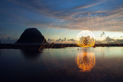 Illuminated ferris wheel by lake against sky at night