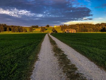 Dirt road amidst field against sky