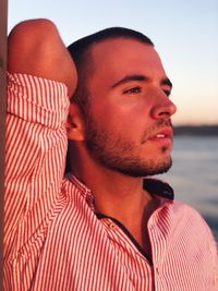 Close-up of thoughtful young man looking away against sky during sunset