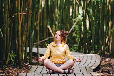 Young woman relaxing among the bamboo tress. sitting in meditation pose.