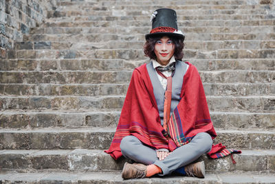 Portrait of man cosplaying mad hatter sitting on staircase against brick wall