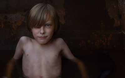 Skinny boy bathing in a rusty container and looking intensely at the camera