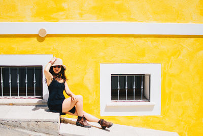Portrait of smiling young woman standing against yellow house