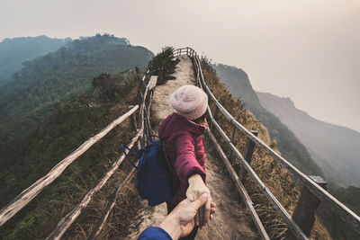 Woman holding person hand on mountains against sky during winter