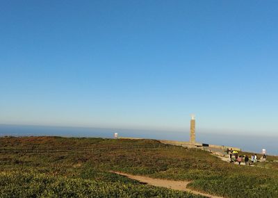 Scenic view of field by sea against clear blue sky