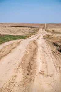 Dirt road passing through landscape against clear blue sky
