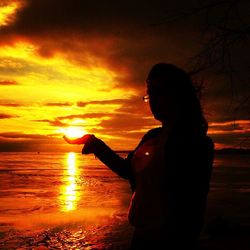 Silhouette of woman standing on beach at sunset