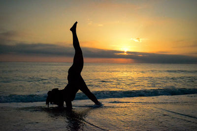 Silhouette man with arms outstretched on beach against sky during sunset