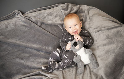 Smiling newborn baby boy sitting with panda toy on gray blanket