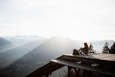 Side view of unrecognizable female tourist sitting at viewpoint in mountains and observing amazing scenery in morning