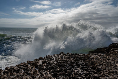 Waves splashing on rocks against sky