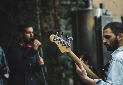 Side view of young man playing guitar in city