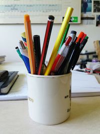 Pencils and pens in mug on table