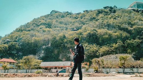 Side view of young man standing on road against mountain during sunny day