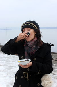 Woman eating seafood against lake during winter