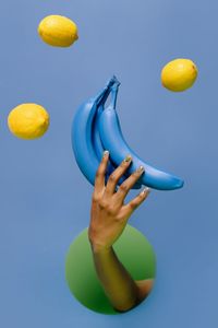 Close-up of hand holding fruit against blue background