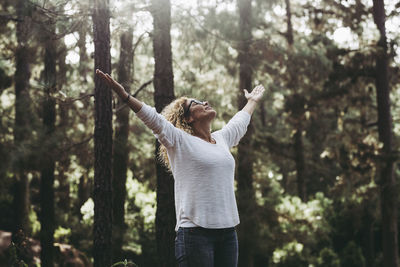 Rear view of woman with arms raised standing in forest