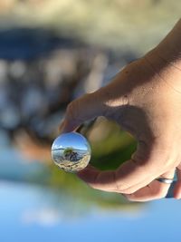 Close-up of hand holding crystal ball against sky