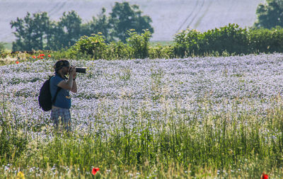 Man photographing flowers on field