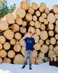 Mid adult man standing against stacked logs on snow covered field during winter