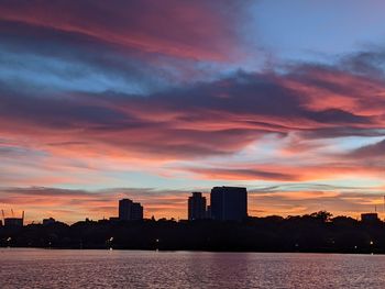 Scenic view of river by buildings against sky during sunrise