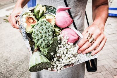 Midsection of woman holding flowers while standing on footpath